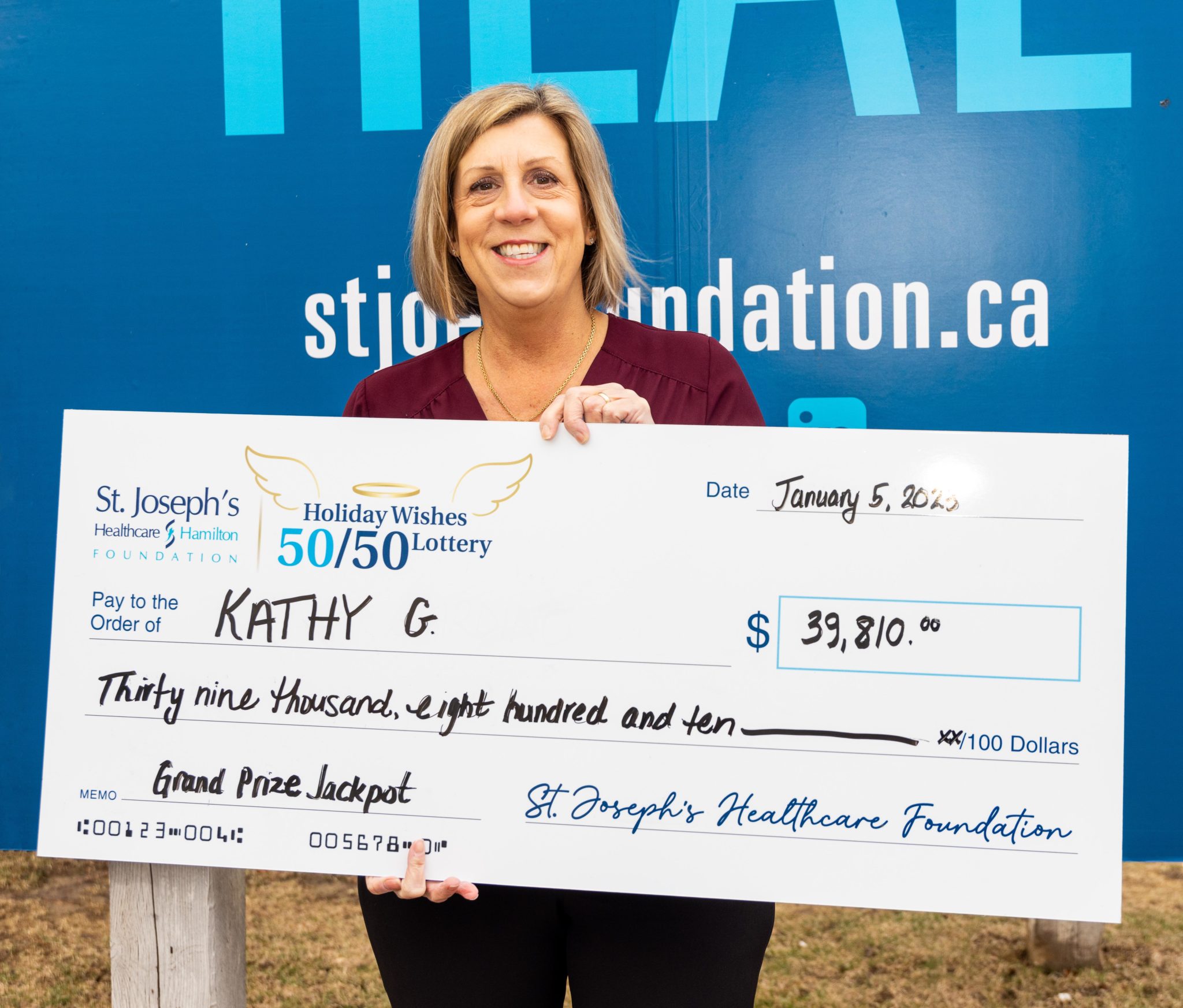 Holiday Wishes Lottery Winner, Kathy G., smiles while holding an oversized novelty cheque with her name on it for $39,810.00