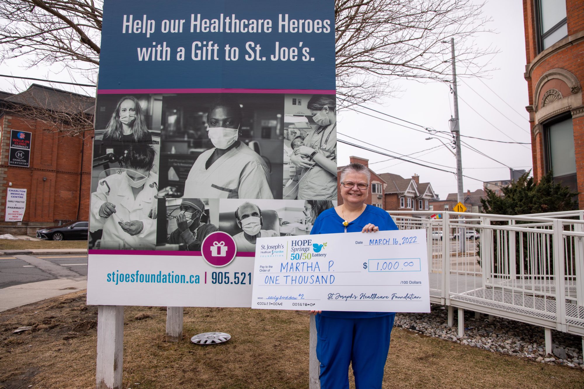 A nurse smiles while holding up a large cheque for $1,000.